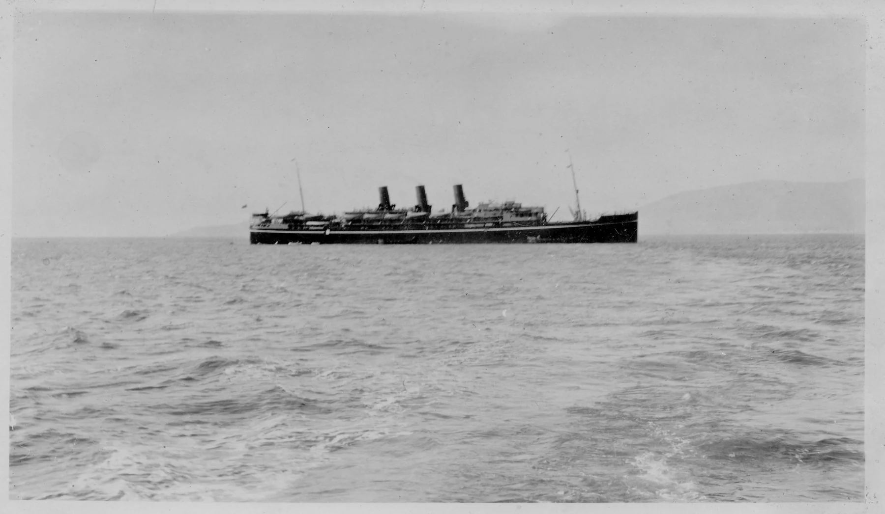 The SS Narkunda, a three-funnelled P&O liner, lying off Gibraltar with hills behind and open water in front.