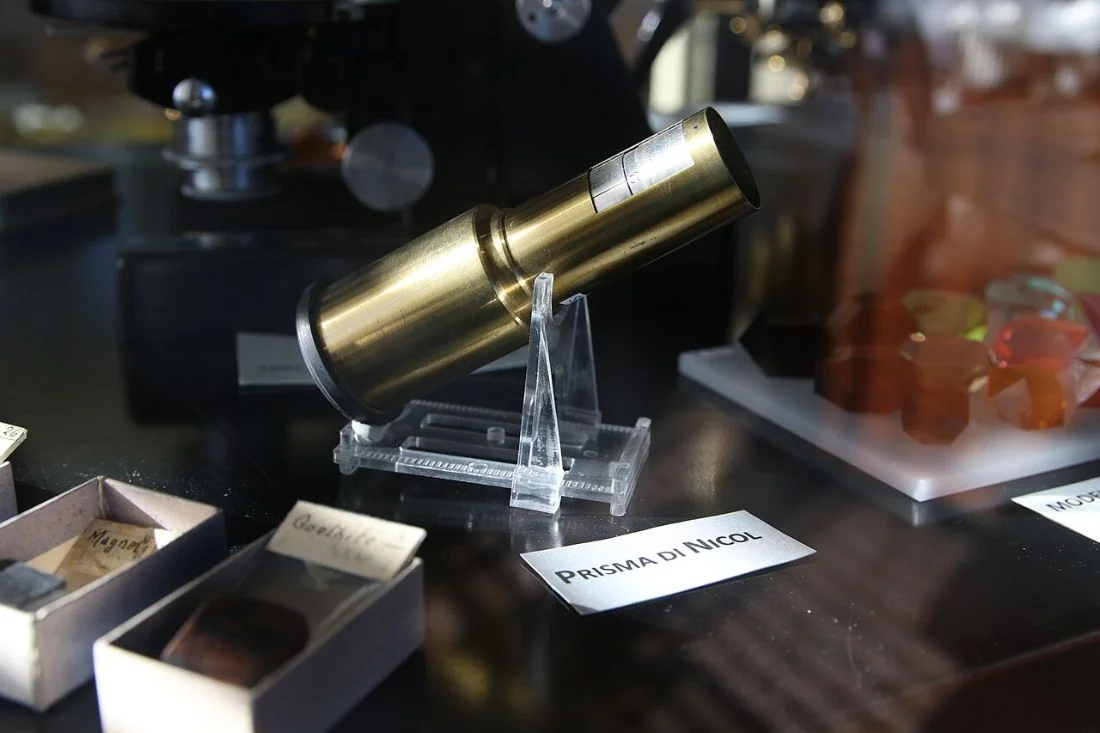 A brass-mounted Nicol prism on a small stand in a museum case, with a label reading Prisma di Nicol.