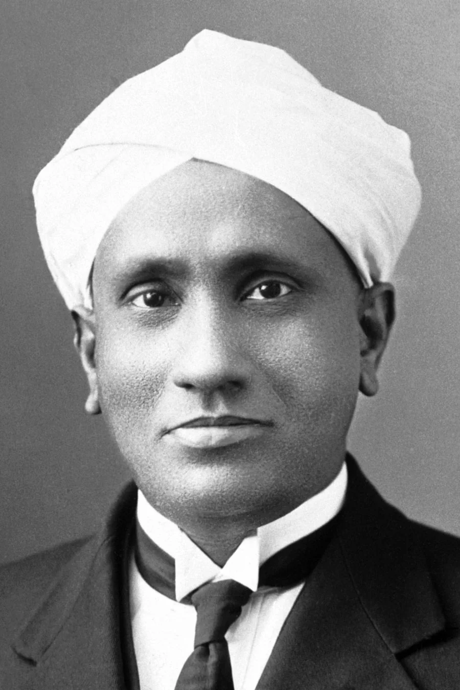 Studio portrait of C. V. Raman in a white turban, dark coat and tie.