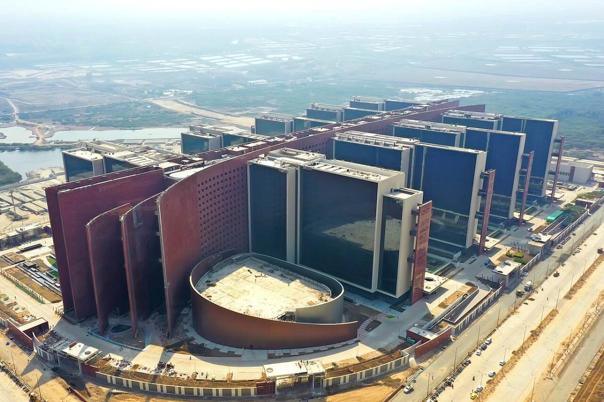 Aerial view of a vast complex of interlinked office towers on flat land at the edge of a city.